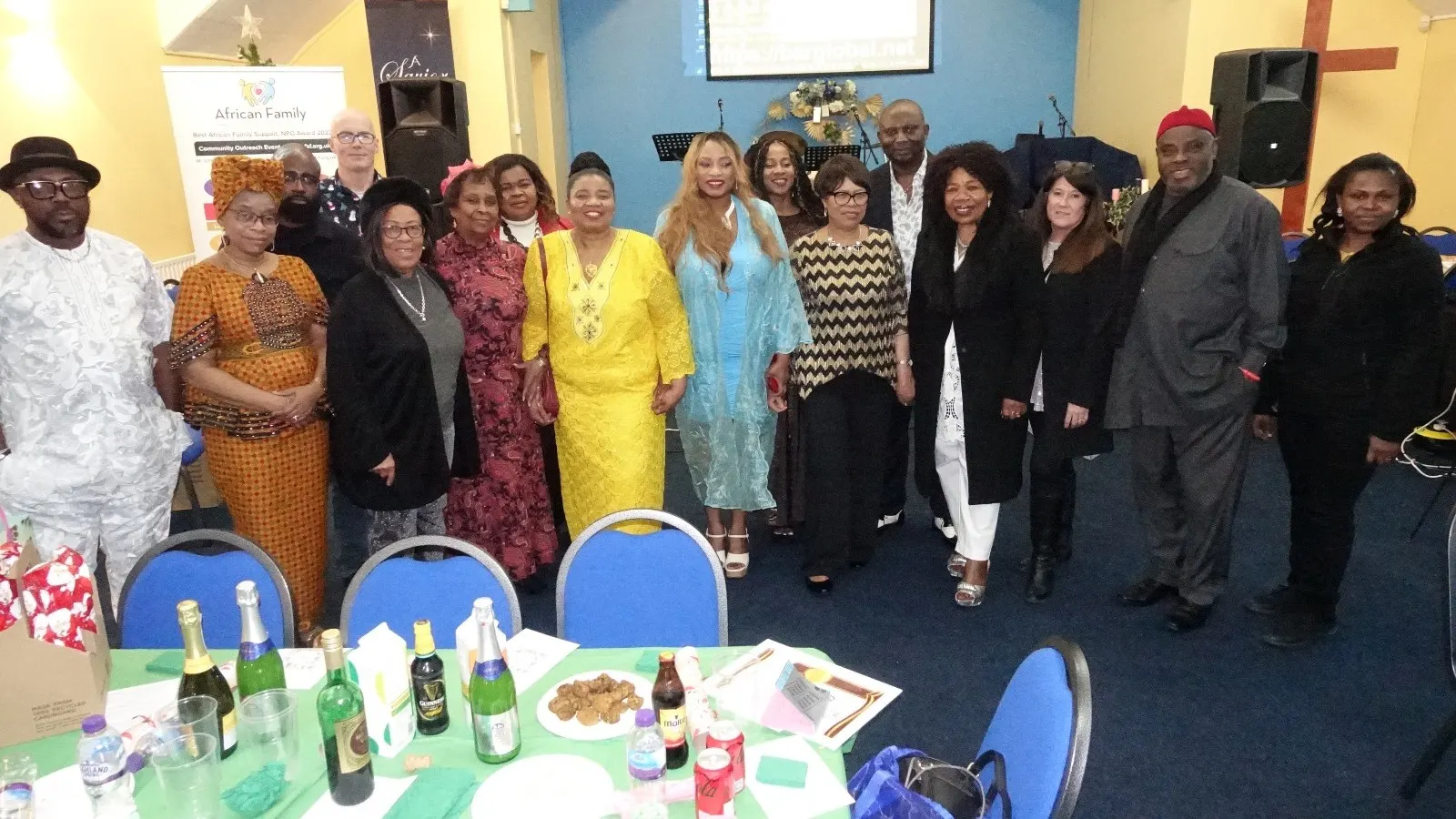 A large group of community members, volunteers, and staff posing together in a church hall next to the African Family Support Foundation banner.